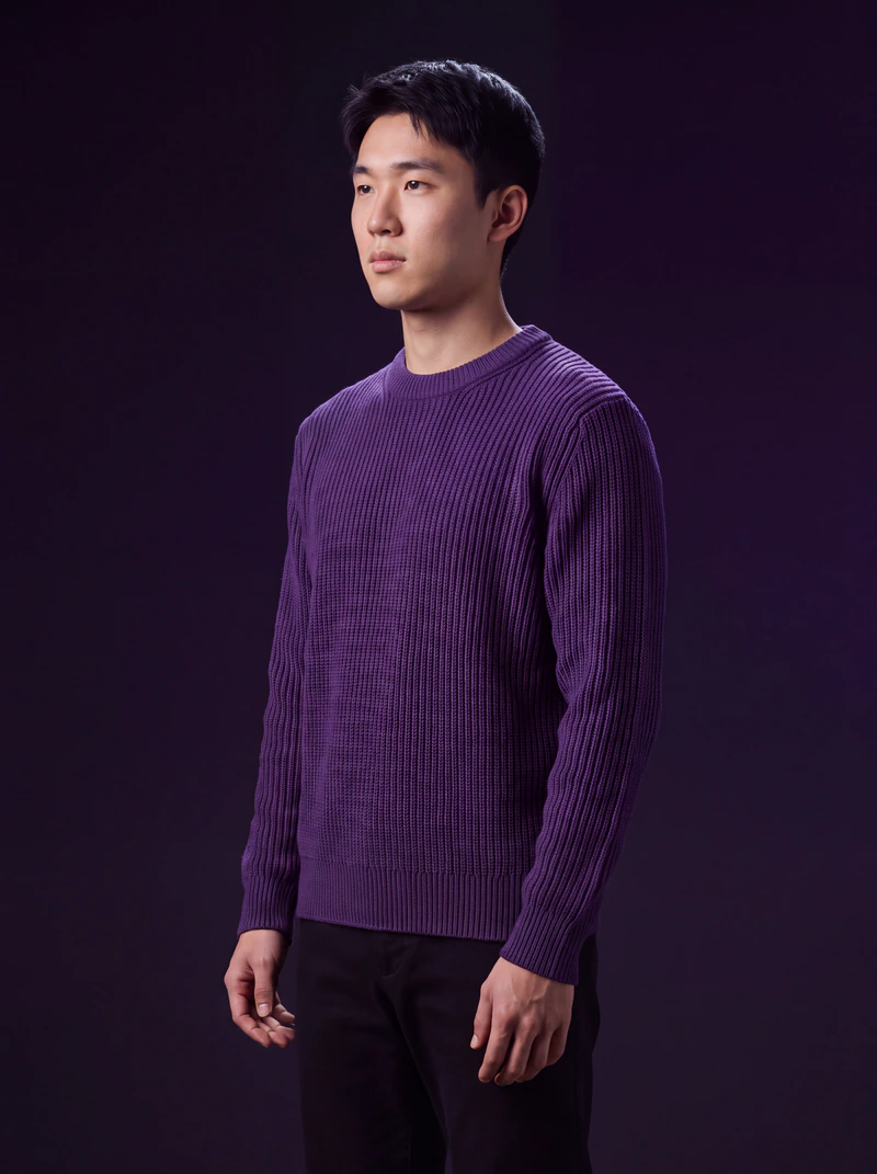 A man wearing the violet sweater in a dark studio